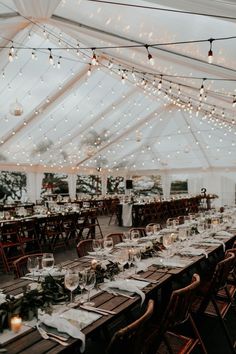 an indoor tent with tables and chairs set up for a wedding reception under string lights