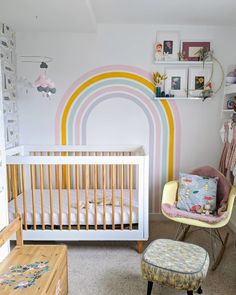 a baby's room with a crib, rocking chair and rainbow wall mural