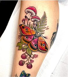 a colorful butterfly and mushrooms tattoo on the right leg, with leaves and berries around it