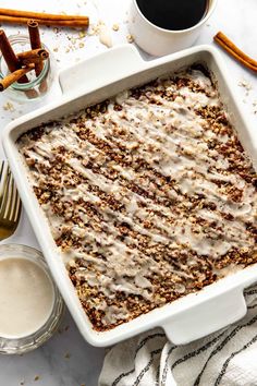 a baking dish filled with cinnamon rolls and topped with icing next to a cup of coffee