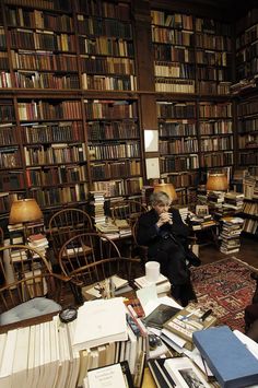 a woman sitting in a library with lots of books on the floor and shelves full of books