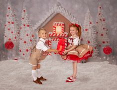 two young children are posing in front of a gingerbread house with presents on it