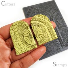 a hand holding a pair of yellow and black square shaped wooden buttons with intricate designs on them