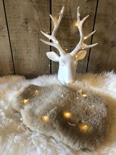 a white deer head with christmas lights on it's antlers sits on a fur rug