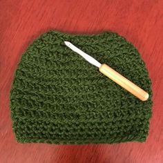 a crocheted green hat with a wooden handle on a table next to a pair of scissors