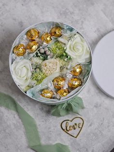 a bowl filled with flowers and chocolates next to a box of love written in gold foil