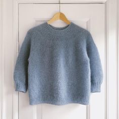 a blue sweater hanging on a white door with a wooden hanger in front of it