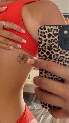 a woman with a flower tattoo on her stomach holding a cell phone and taking a selfie