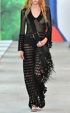 a woman walking down a runway wearing a black dress with fringes on the skirt