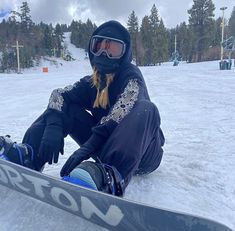 a woman sitting in the snow with her snowboard