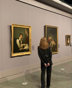 a woman looking at paintings on display in a museum