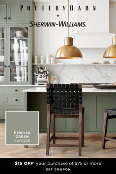 two chairs are sitting in front of a counter with green cabinets and gold pendant lights