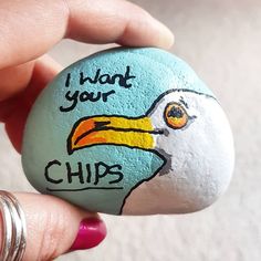 a hand holding a painted rock with a bird's head and words on it