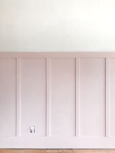 an empty room with white paneling and wood flooring on the wall, in front of a light switch