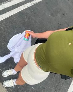 a woman in green shirt and white skirt standing next to a person with an orange can