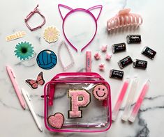 the contents of a pink bag are laid out on a marble table with pens, scissors and other items