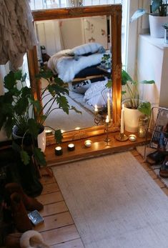 a mirror sitting on top of a wooden floor next to a potted plant and candles