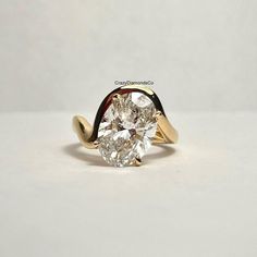 a ring with a large diamond in the center on a white surface, it is gold and has a curved band