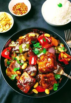 a black plate topped with meat and veggies next to bowls of rice on a table