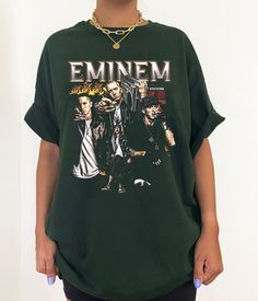 a woman standing in front of a white wall wearing an eminem shirt and black shorts