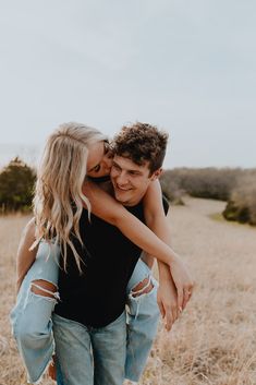 a young man and woman hugging each other while standing in the middle of a field