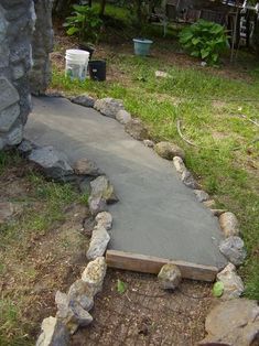 a cement walkway in the middle of a yard with rocks around it and a trash can on the other side