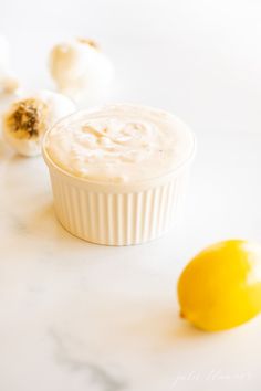 a small white bowl filled with food next to an orange and two garlic cloves