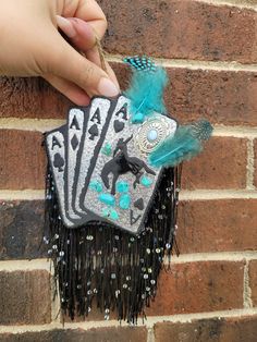 a hand holding four playing cards with blue feathers and black horses on them, against a brick wall