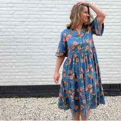 a woman standing in front of a white brick wall wearing a blue floral print dress