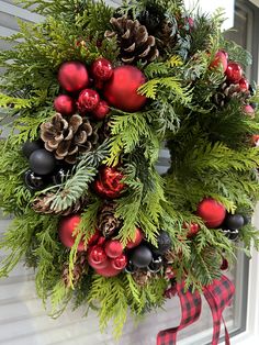 a wreath with pine cones and ornaments hanging from the side of a house on christmas day