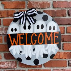 a welcome sign with ghost faces hanging on a brick wall