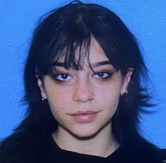 a young woman with black hair and piercings looks at the camera while wearing a black shirt