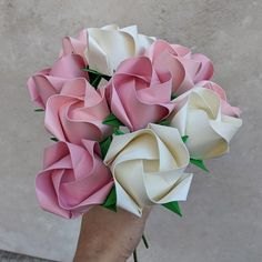 a hand holding a bouquet of pink and white paper roses with green leaves on it