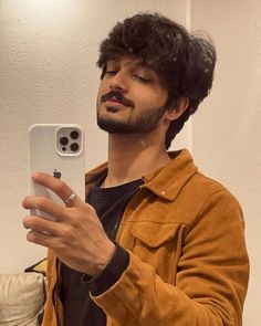 a man taking a selfie with his cell phone in front of him and wearing a brown jacket