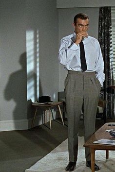 a man in a dress shirt and tie standing in a living room next to a coffee table