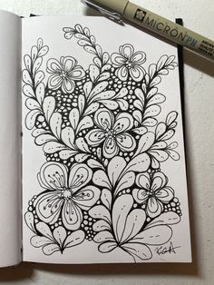 an open notebook with a drawing of flowers and leaves on the page next to a marker pen