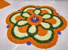 an orange, white and purple flower design on the ground with a candle in it