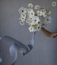 a bouquet of daisies being held by someone's hand with a gray ribbon