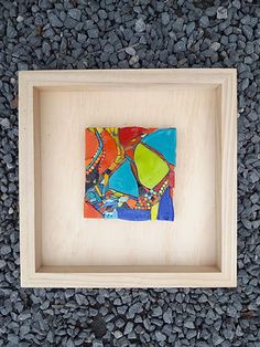 a wooden frame with a colorful painting on the front and bottom, sitting on gravel