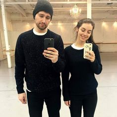 a man and woman standing next to each other holding up cell phones in an empty room