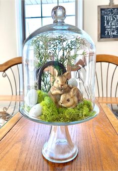 a glass clochel filled with plants and animals under a dome on top of a wooden table