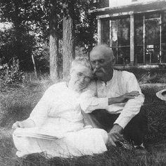 an old black and white photo of two people sitting next to each other in the grass