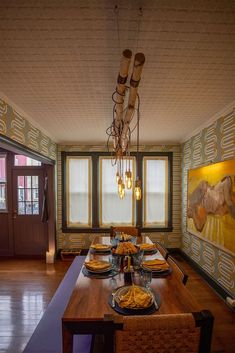 a dining room table with plates and utensils on it, in front of two windows