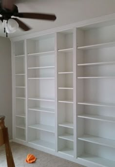 an empty room with white bookcases and a ceiling fan