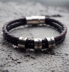 a leather bracelet with two silver beads on top of cement ground and the word love is written in three different languages