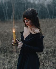 a woman in a black dress holding a lit candle