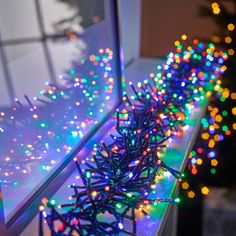 a window sill filled with lots of christmas lights next to a small fir tree