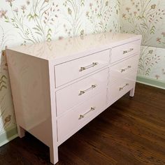 a white dresser sitting on top of a hard wood floor next to a wallpapered wall