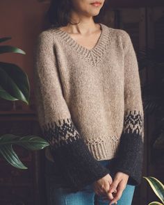 a woman standing next to a potted plant wearing a sweater with geometric designs on it