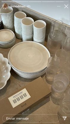 a table topped with lots of white dishes and cups next to a cardboard box filled with empty glasses